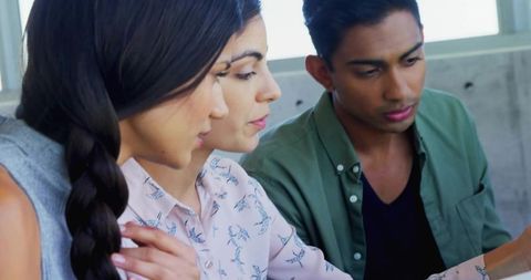 Collaborating young professionals reviewing mobile device in bright coworking space