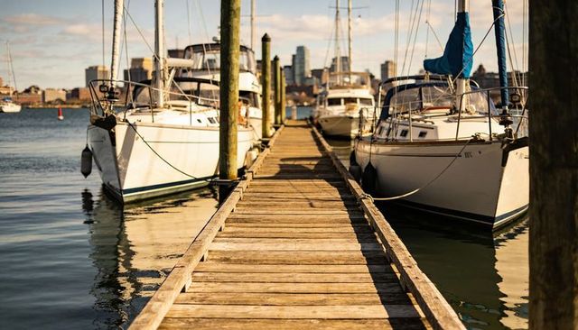 Wooden dock leading into marina with sailboats and city skyline at golden hour