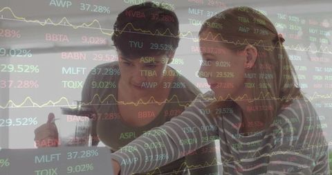 Two women collaborating over laptop analyzing stock tickers and financial data on screen
