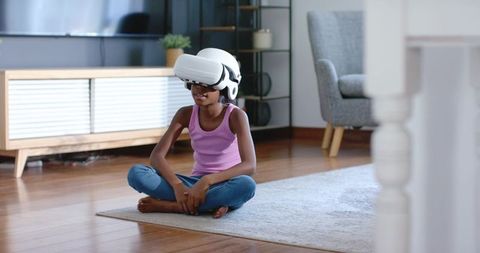 African american girl experiencing virtual reality while sitting cross-legged on rug