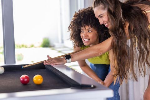 Multiracial women playing pool and laughing in bright living room leisure lifestyle