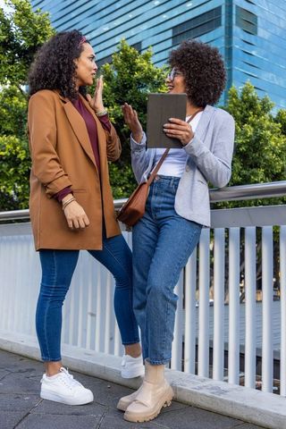 African american women chatting and collaborating on urban bridge holding tablet