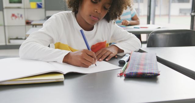 Image of african american schoolboy sitting at desk writing in school class. Education, childhood, inclusivity, elementary school and learning concept.