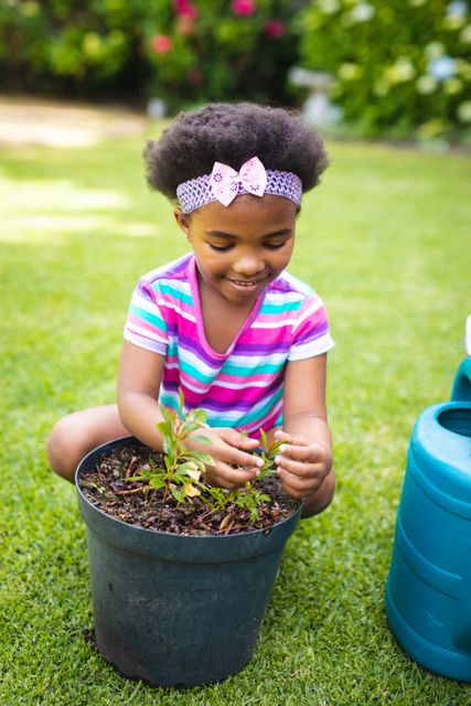 Smiling african american girl looking at potted plant while gardening in backyard. unaltered, nature, childhood and gardening.