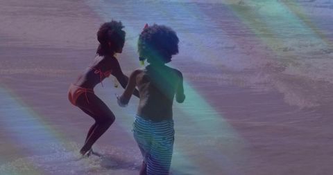 Children splashing at shoreline with snorkel and rainbow light streaks, summer seaside play