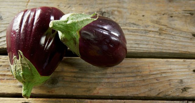 Shows two fresh eggplants resting on a wooden surface. Useful for topics related to organic farming, healthy vegetables, natural produce, and cooking ingredients. Suitable for food blogs, online grocery stores, and agricultural websites.