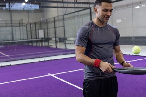 Man playing paddle tennis on indoor purple court catching ball while holding racket