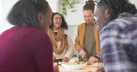 Friends laughing while chopping vegetables at kitchen island preparing salad together