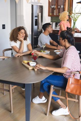 Multicultural friends gathering around kitchen table casual sharing snacks and conversation
