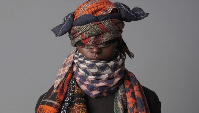 Posing model wearing layered patterned scarves and headwraps covering eyes, textile styling
