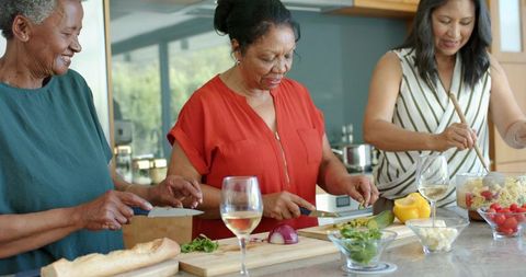 Chopping and stirring together diverse women preparing fresh meal in bright modern kitchen