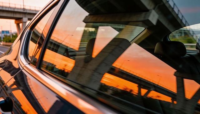 Reflecting sunset on dark sedan rear door and window under urban overpass