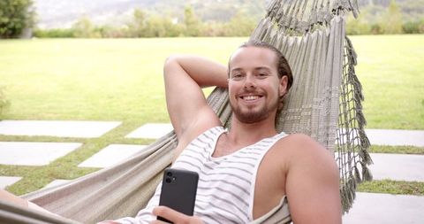 Relaxed young man in hammock enjoying smartphone outdoors