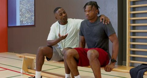 Coach advising athlete on bench in indoor gym coaching session focusing on motivation