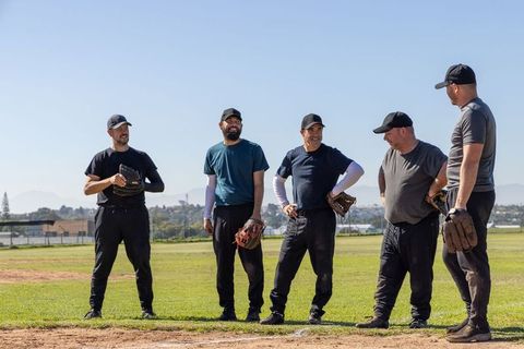 Casual men baseball team chatting between plays on sunny field wearing caps and mitts