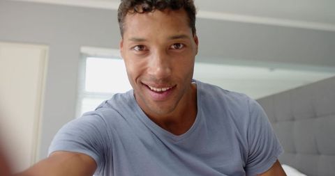 Smiling man holding smartphone on bed in minimalist bedroom