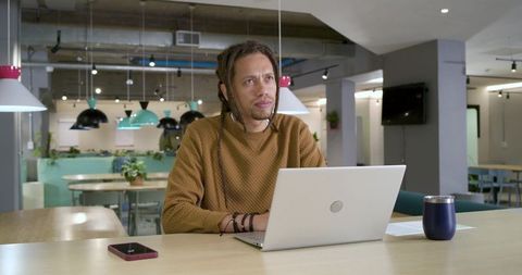 Contemplative african american man working on laptop in modern coworking space