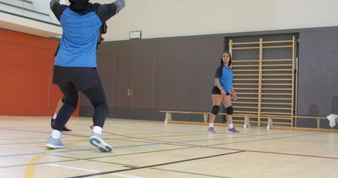 Diverse female athletes practicing volleyball drills in gym wearing knee pads, sportswear