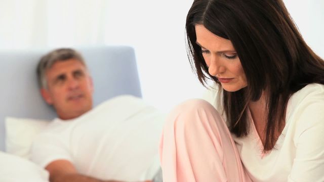 Middle aged couple deep in thought in bedroom, each displaying contemplative expressions. Useful for depicting emotional moments in relationships, communication challenges, intimacy in mature relationships, or mental well-being in couples. Ideal for use in articles, blogs, marketing materials related to marriage counseling, relationship advice, mental health, and family life.