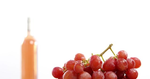 A bunch of red grapes is in focus in the foreground, with a blurred orange bottle in the background, with copy space. Grapes are often associated with health and wellness, and the contrasting colors add a vibrant touch to the composition.
