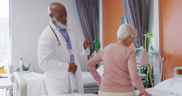 African american male doctor examining the back of senior caucasian female patient at hospital. Medicine, healthcare, lifestyle and hospital concept.