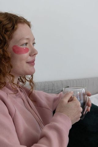 Relaxing on sofa holding double-wall mug with under-eye hydrogel patch