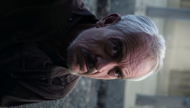 Moody closeup portrait of elderly man reclining on urban pavement with weathered coat