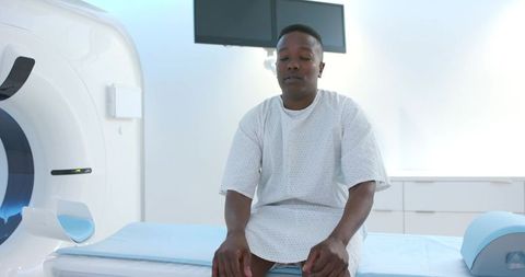 Male patient sitting on ct scanner table wearing hospital gown preparing for scan