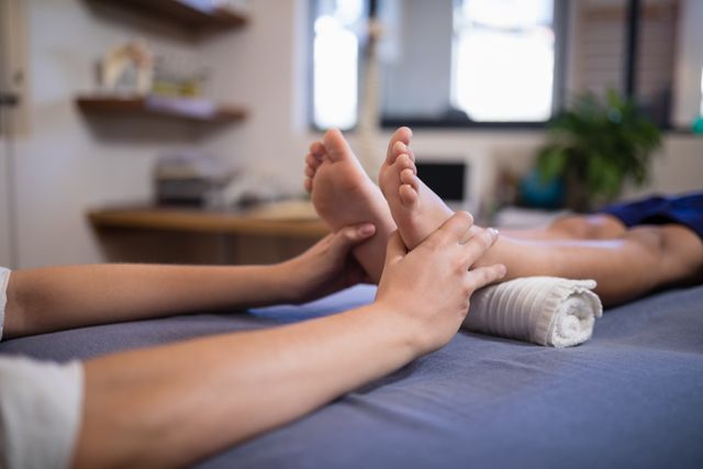 Child lying on bed receiving foot massage from female therapist in hospital. Ideal for use in healthcare, wellness, pediatric care, and rehabilitation contexts. Can be used in articles, blogs, and promotional materials related to medical treatments, therapy sessions, and child healthcare.