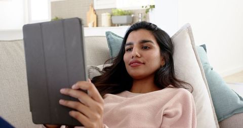 Indian Woman Relaxing on Sofa with Tablet in Modern Home Setting