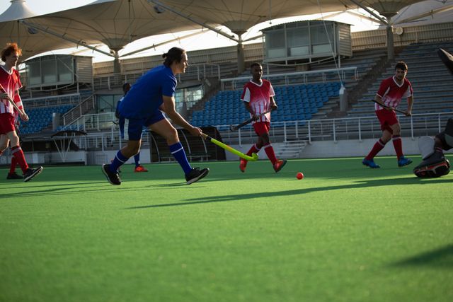 Two multi-ethnic teams of teenage male field hockey players, one player preparing to hit a ball on the pitch during a hockey game. Sport game competition.