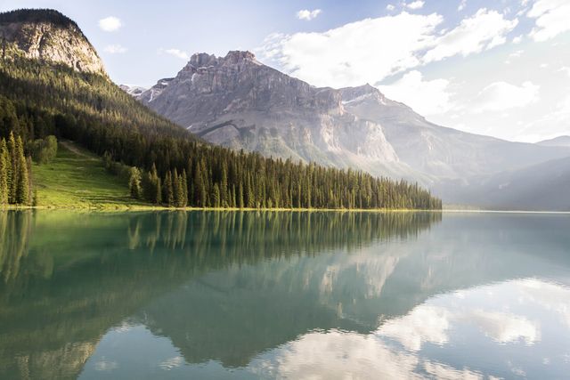 Serene alpine lake reflecting majestic mountains under clear morning light. Evergreen trees create a tranquil atmosphere. Ideal for nature-themed projects, travel brochures, relaxation visuals, and environmental campaigns.