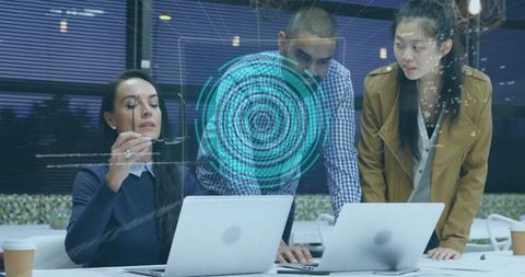 Team collaborating with holographic data interface over laptops in modern office late night