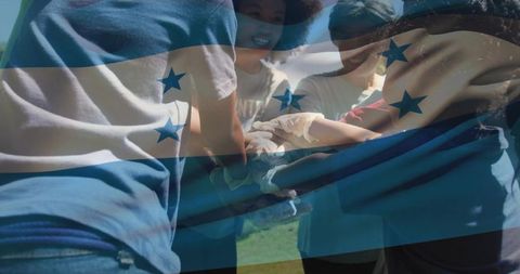 Honduras flag overlay on volunteers stacking hands forming outdoor team huddle showing unity