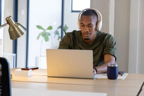 African american man working on laptop wearing headphones in modern minimalist office