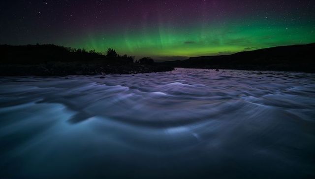 Aurora borealis dancing over swirling river long exposure with silky water and starry sky