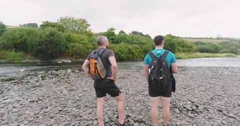 Two Men Walking Along Rocky Riverbank While Hiking - Download Free Stock Images Pikwizard.com