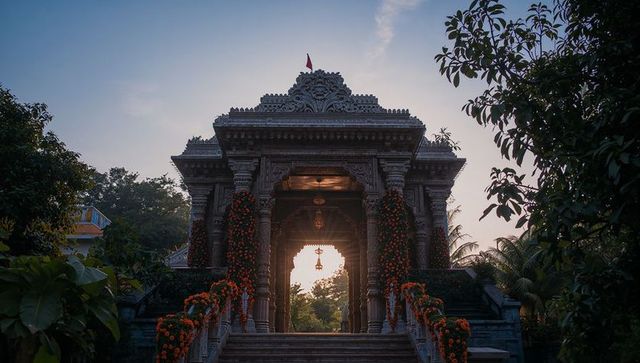 Carved temple gateway illuminating sunrise framed by orange garlands and hanging brass bell