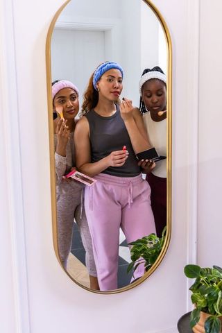 African american friends applying makeup together in cozy home self-care by gold mirror