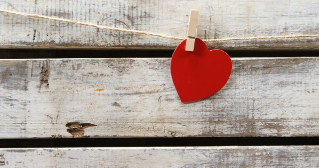 A red heart-shaped cutout is attached to a rustic wooden background with a clothespin, symbolizing love and affection, with copy space. Its simplicity and the contrast of colors make it ideal for themes related to Valentine's Day, romance, or heartfelt messages.