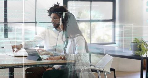 Pointing man guiding woman using laptop and tablet with code overlay in modern office