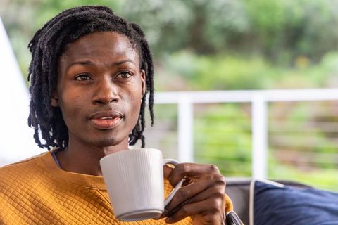 African american man holding mug on balcony wearing mustard sweater contemplating morning calm