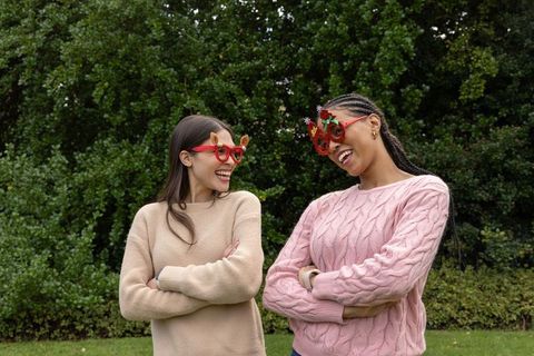 Friends laughing and chatting outdoors wearing festive novelty glasses and knit sweaters