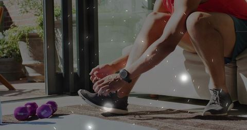 Man tying running shoes at home before workout with purple dumbbells and smartwatch