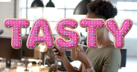Tasty donut text overlay on woman checking smartphone and sipping coffee in modern office