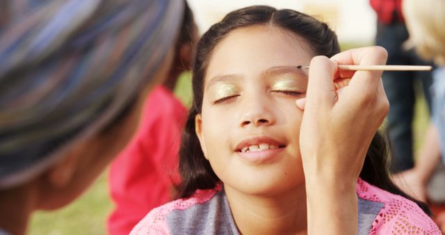 Girl happily receiving face paint with eyes closed at an outdoor festival. Great for themes involving children's activities, festivals, art, and creativity. Illustrates the joy of outdoor festivities and engaging activities.