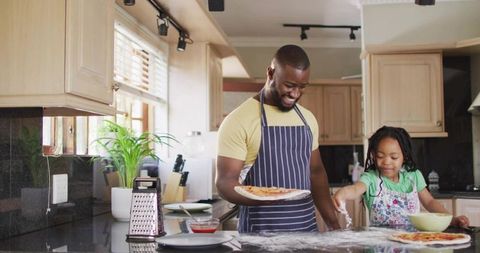 Smiling parent and child making homemade pizza together, sprinkling flour, family cooking