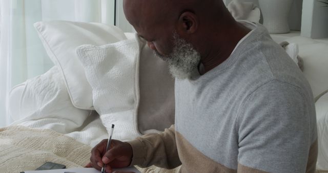 Elderly man writing in a notebook while sitting on a comfortable sofa - Download Free Stock Images Pikwizard.com