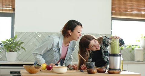 Two friends blending green smoothie in kitchen promoting healthy cooking and wellness