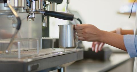 Barista steaming milk for latte art at espresso machine closeup with stainless pitcher